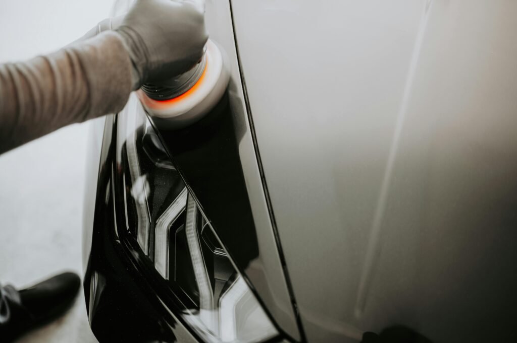 Close-up view of a person polishing a black car using a buffing machine.